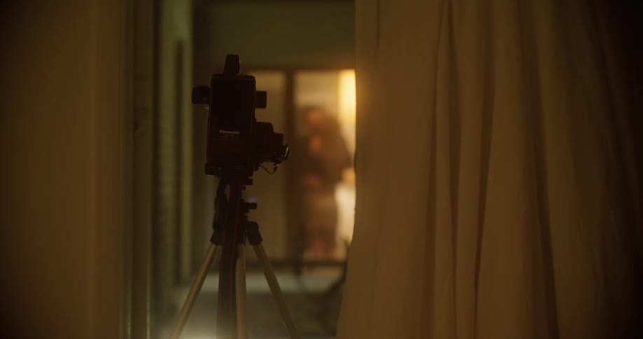 Woman and man kissing behind a textured glass in front of a camera mounted on a tripod