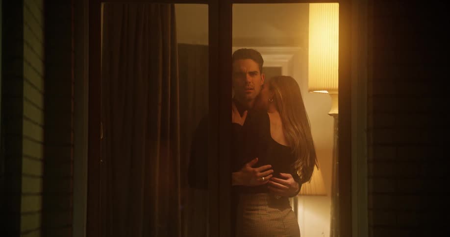 Man looking out doors while cuddling woman closes curtains