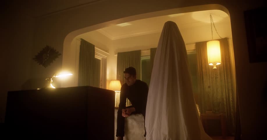 Man sits on bed thinking accompanied by shrouded figure