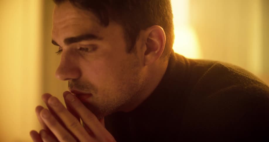 Man with a black turtleneck sweater sitting on a bed feels depressed and rubs his eyes in the bedroom