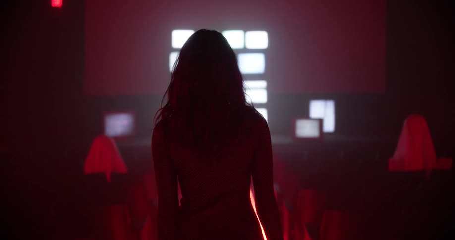 A woman walking in an auditorium with chairs towards a stage with television sets
