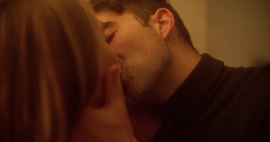 A white man walks over to a woman in a hallway and kisses her
