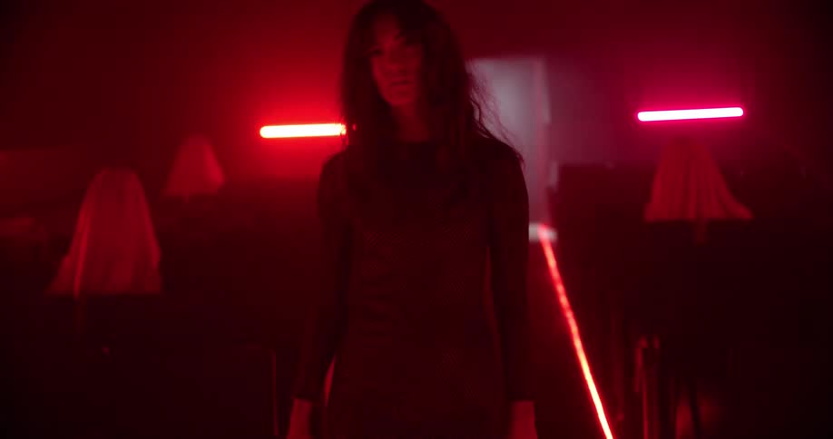 Woman in a long dress walks down a movie theatre under red lights