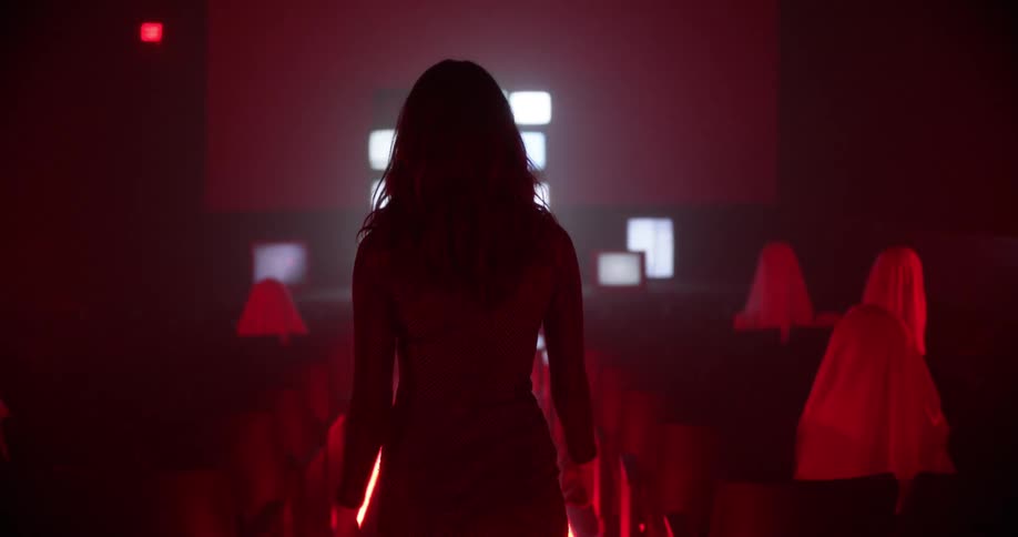 A woman walks through a dark theater with televisions on the stage