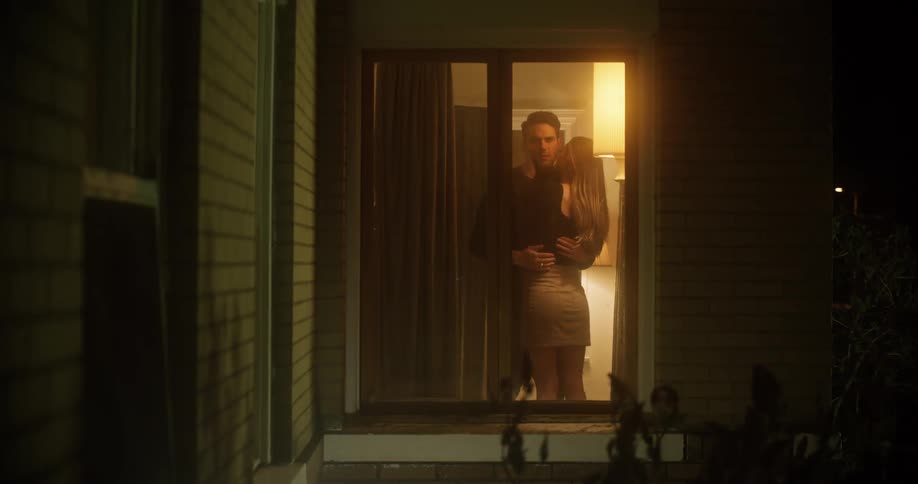 A man looks off in the distance as his girlfriend kisses his neck