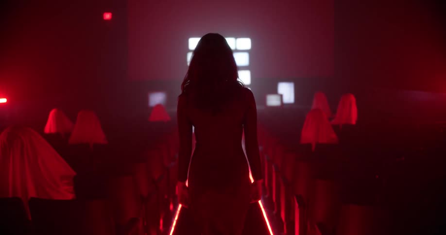 Woman in a long dress on a movie theater under red lights towards television screens showing static
