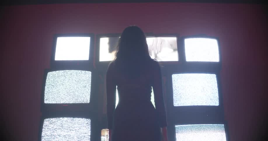 Silhouette of a woman standing in front of tv screens with white noise
