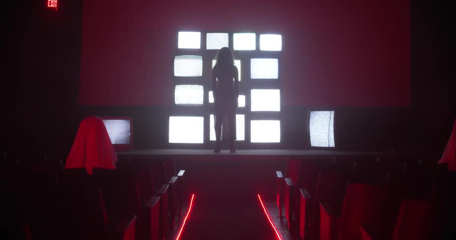 The silhouette of a woman on stage standing in front of stacked and glowing screens in an empty theater