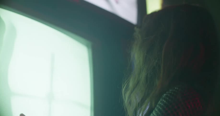 A woman sings near a wall of televisions
