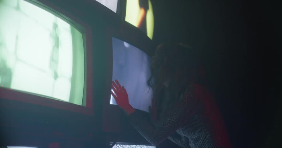A woman singing in front of tv screens while touching them