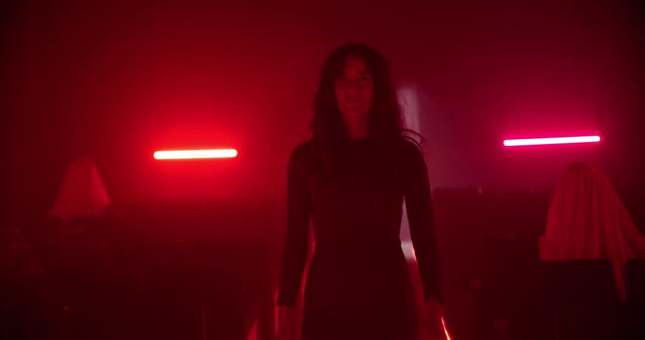 Woman wearing long dress walks down a movie theatre under red lights