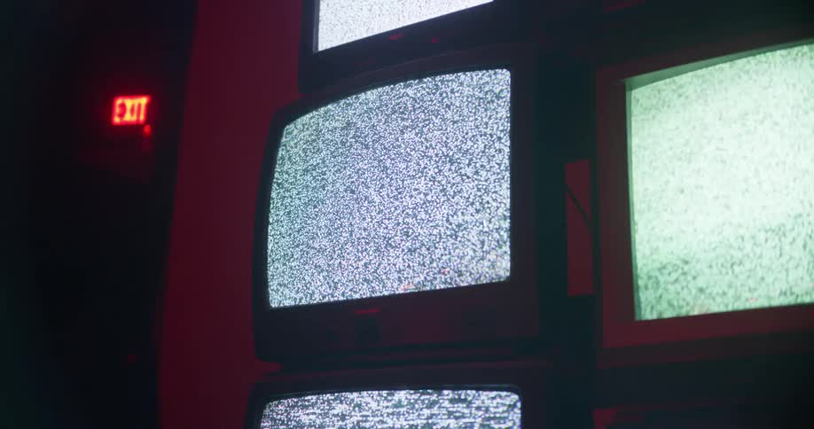 A stack of old televisions display static in a room dimly lit with red lighting