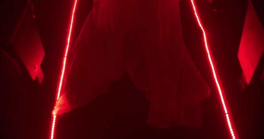A wedding gown is dragging down an aisle in a dark room with glowing red lights