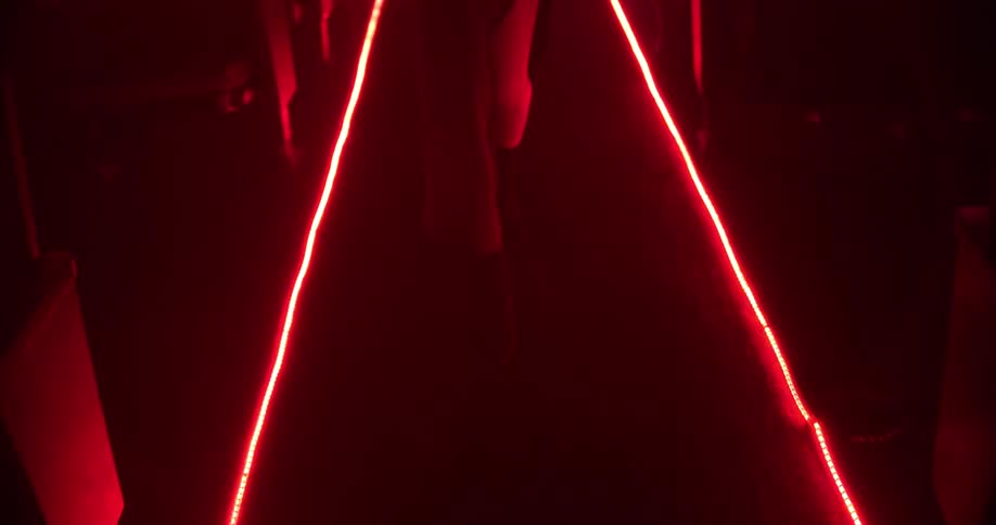 Woman in a long dress walks down the aisle of a theatre under red light
