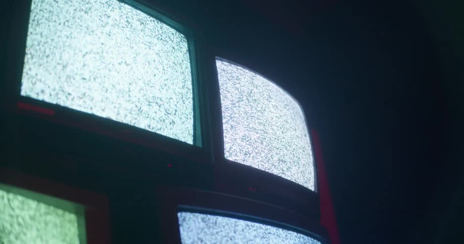 Four television sets play static in a darkened room