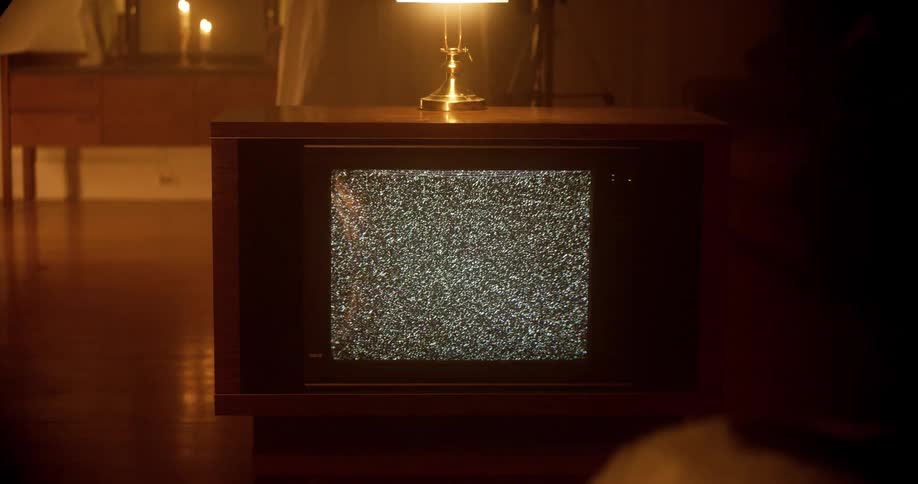A television set with snow on the screen with a lamp on top and a mirror in the background