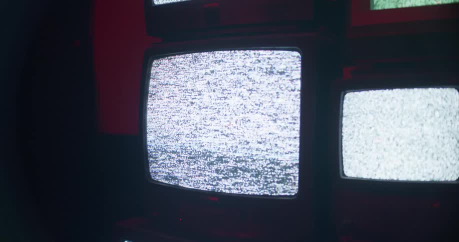 Televisions stacked next to each other and on top of each other play static in a dark room