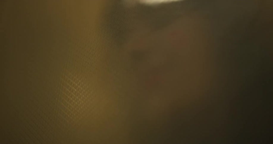 Close up of a womans face through textured patterned glass with red and yellow lights