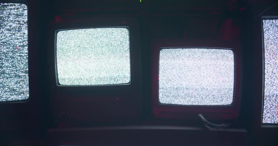 Television screens on a shelf showing static in a dark room