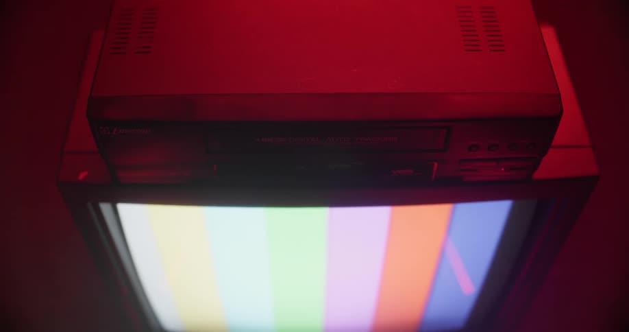 A white person removes a tape from a vhs machine sitting on top of a television