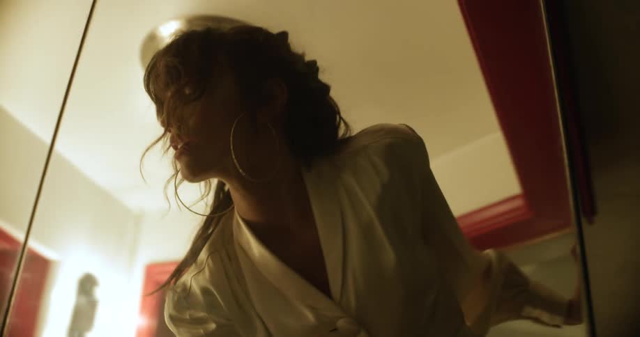 A dark haired white woman dances in a small room encased in glass