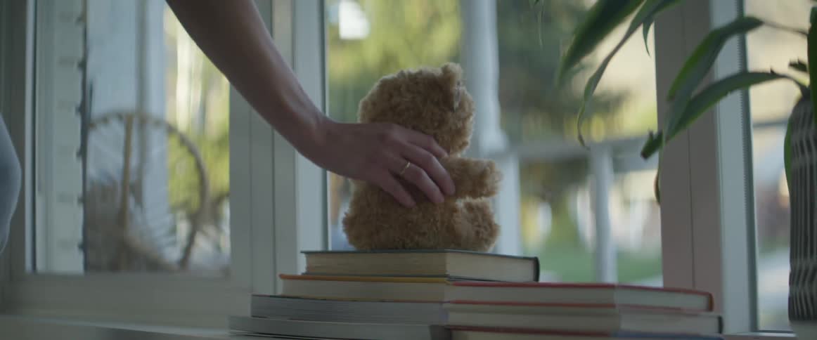Woman places a teddy bear over a pile of books in front of a window