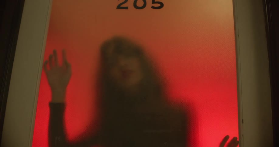 A white woman dances while pushing herself up against the glass pane in a door