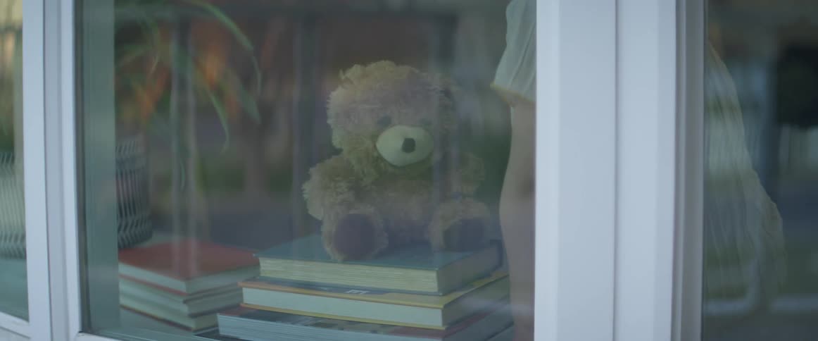 Child places teddy bear on stack of books in front of bay window