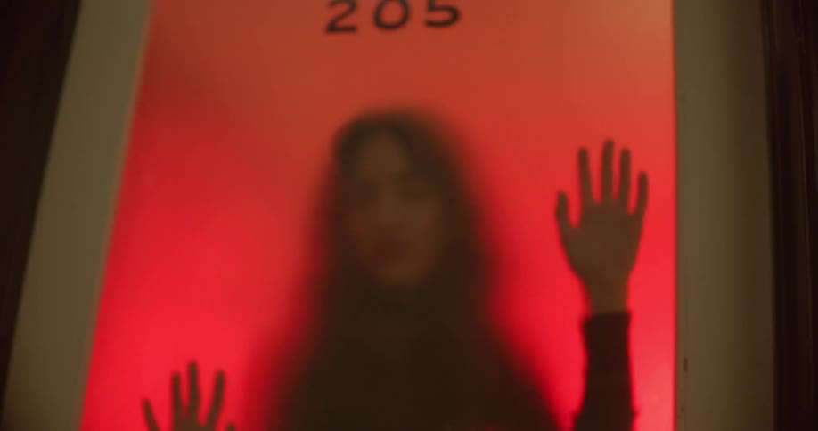 A white woman dances while pressed up against a pane of glass in a door