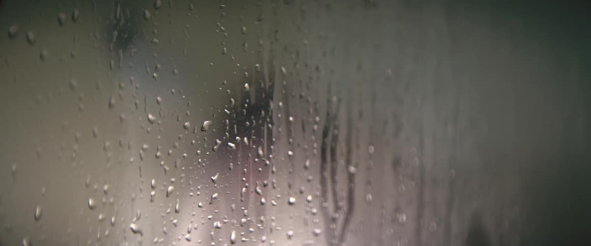 A person takes a shower as steam and water rivulets cling to the glass door