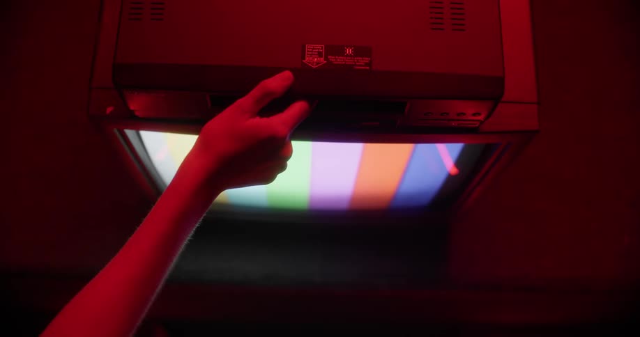 A white person puts a vhs tape into a machine on a television showing a test pattern