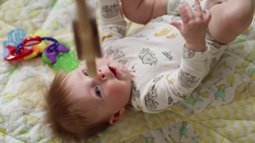 A baby laying down playing with his feet looking at a mobile