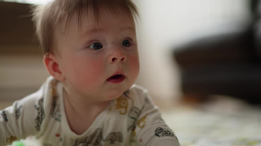 A baby on the floor looks ahead