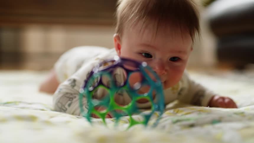 A baby on the floor smiling next to a toy