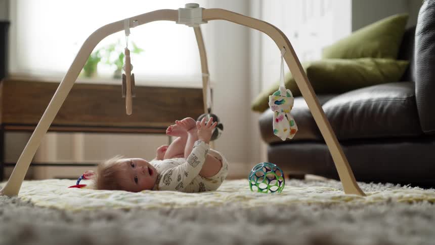 A baby smiles and pulls their feet up in the air while lying on a rug under a mobile