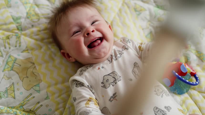 Happy baby laughing and wiggling under a floor mobile
