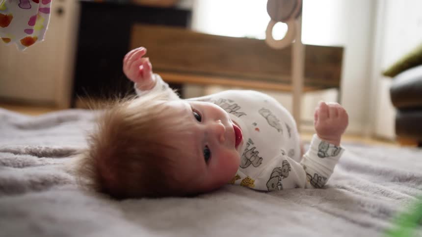 A baby rolls about on a blanket in a living room