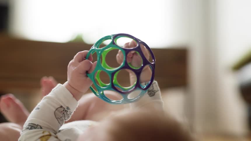 A baby plays with a spherical toy while lying on its back