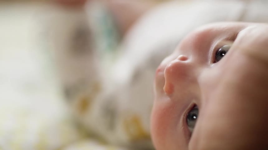 An infant lays in a bed and holds a small ball toy