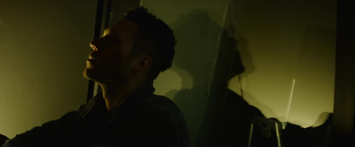 Man sitting on the floor reclines against a window on a dimly lit room