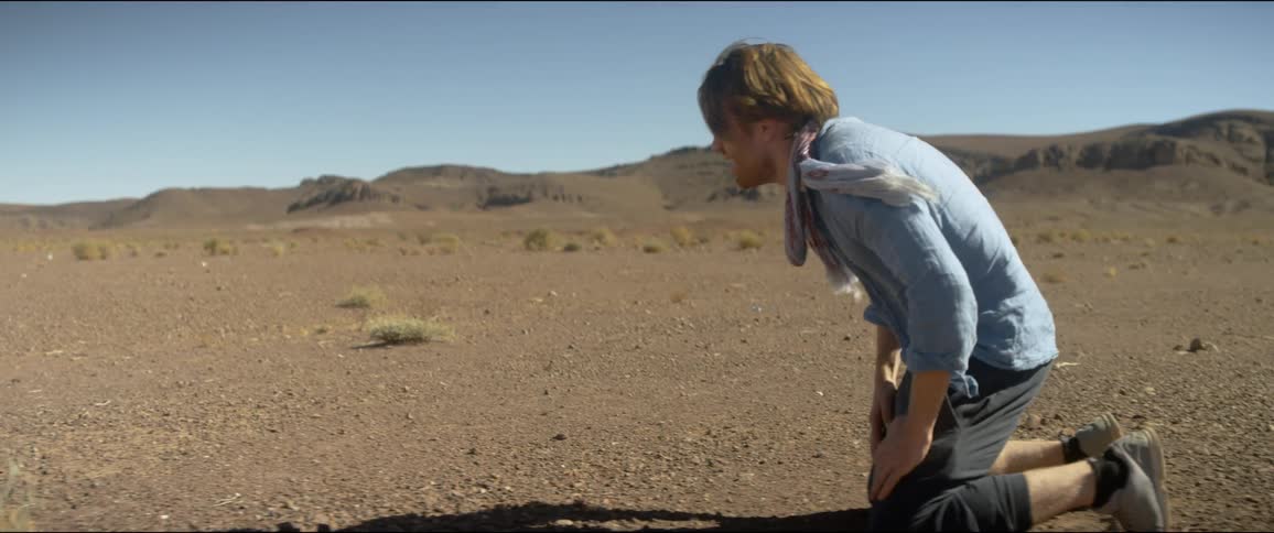 A man falls to his knees while walking in the desert