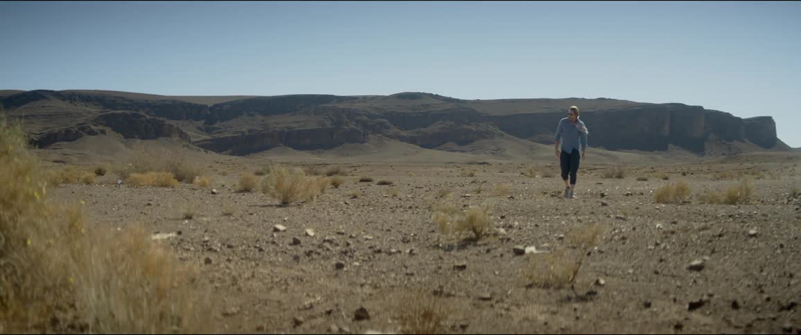 Man walks on the hot sands of a desert near a mesa