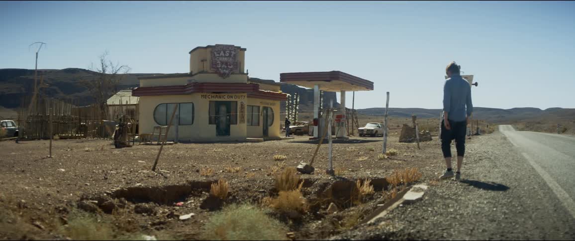 Young man walks towards retro style roadside gas station on deserted highway