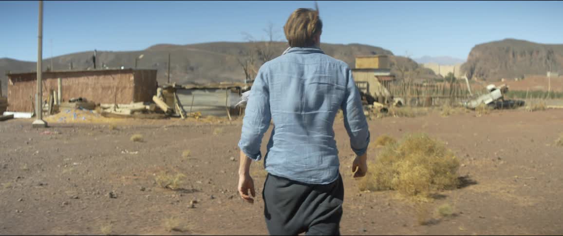 A man walks across some barren ground toward a building