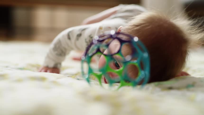 A baby rolls back and forth on a white blanket