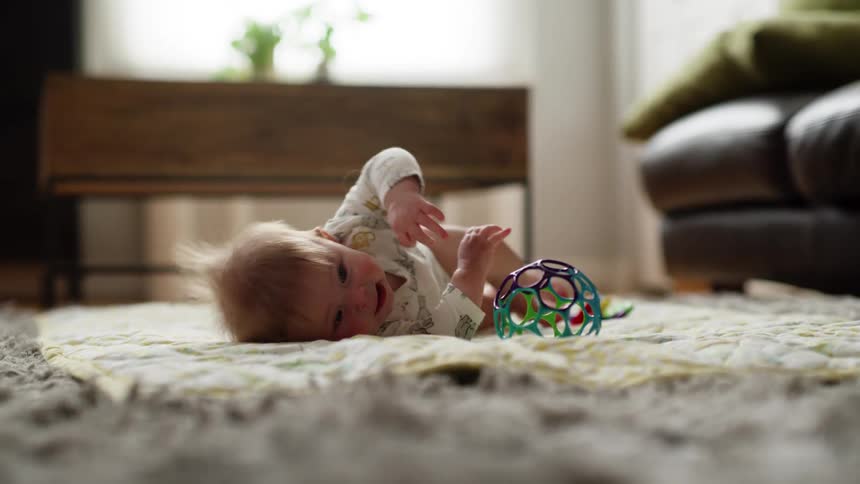 A baby with a toy is on his tummy on a bed and laughs and rolls over