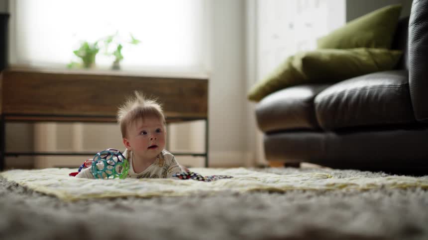 Infant doing tummy time laying on rug with toys