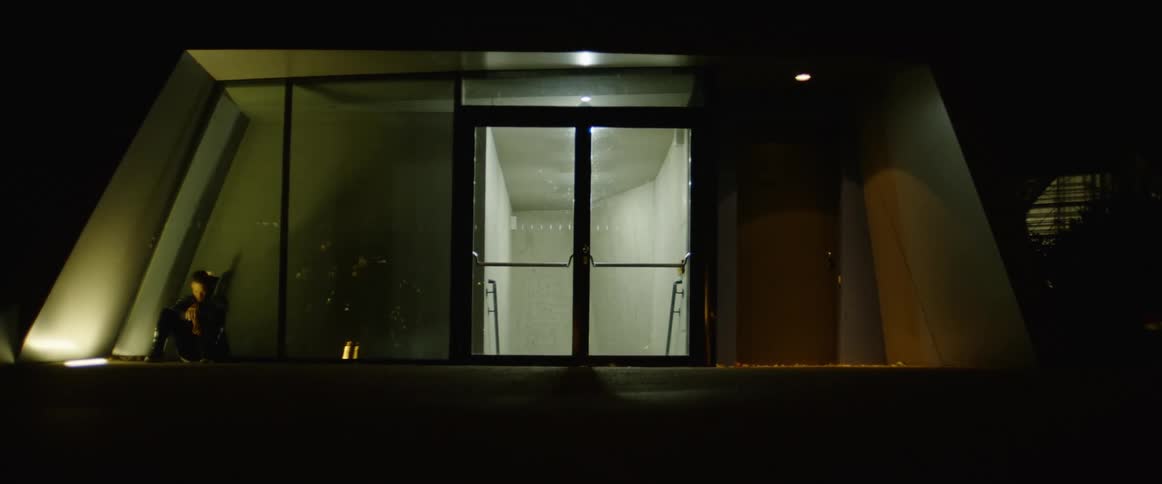 A white man sits near an entrance to a building