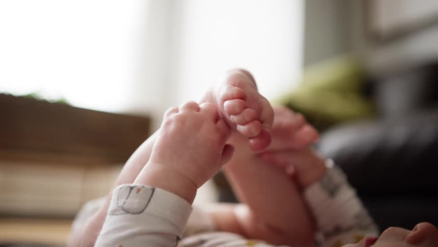 Baby laying on blanket playing with his feet in living room
