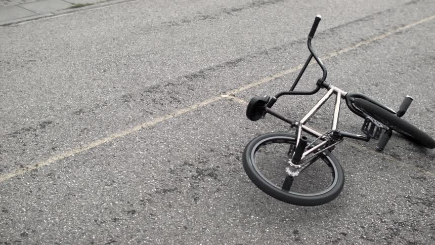 A bike lying in the street with the wheel spinning and a person passes by